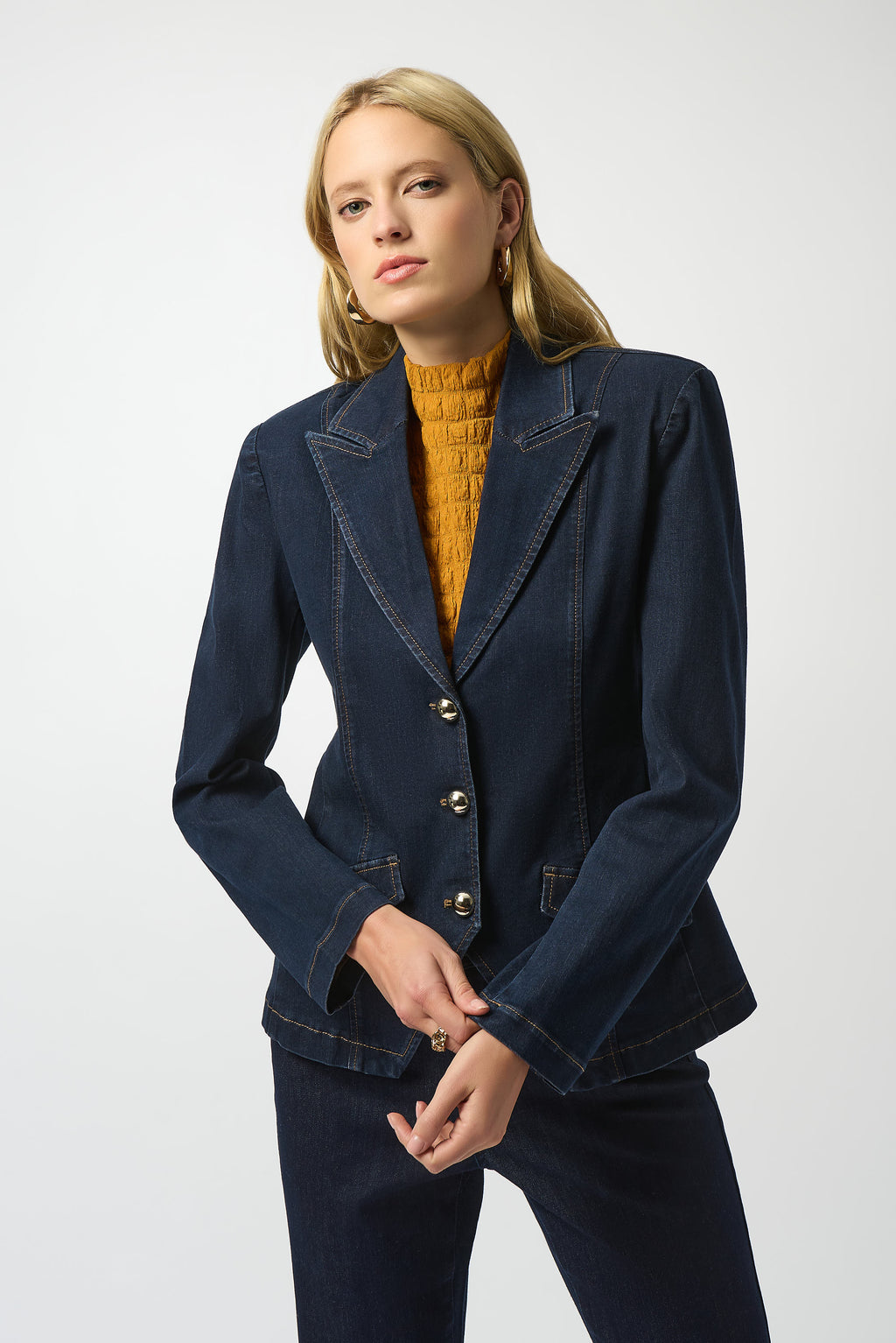Woman wearing a navy blue jacket and pants with a mustard yellow top on a white background