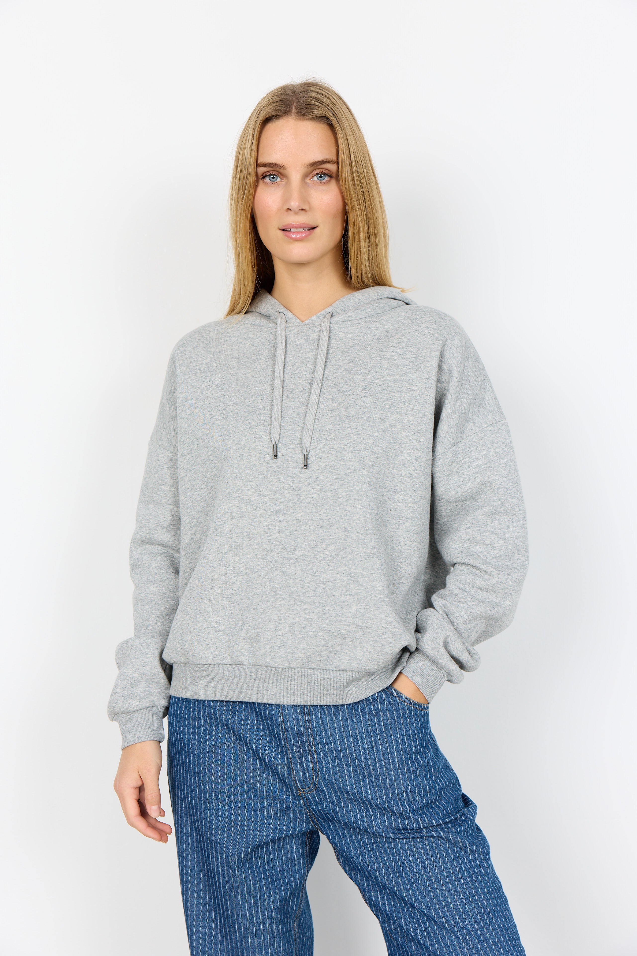 Woman wearing a gray hoodie and blue pants on a white background