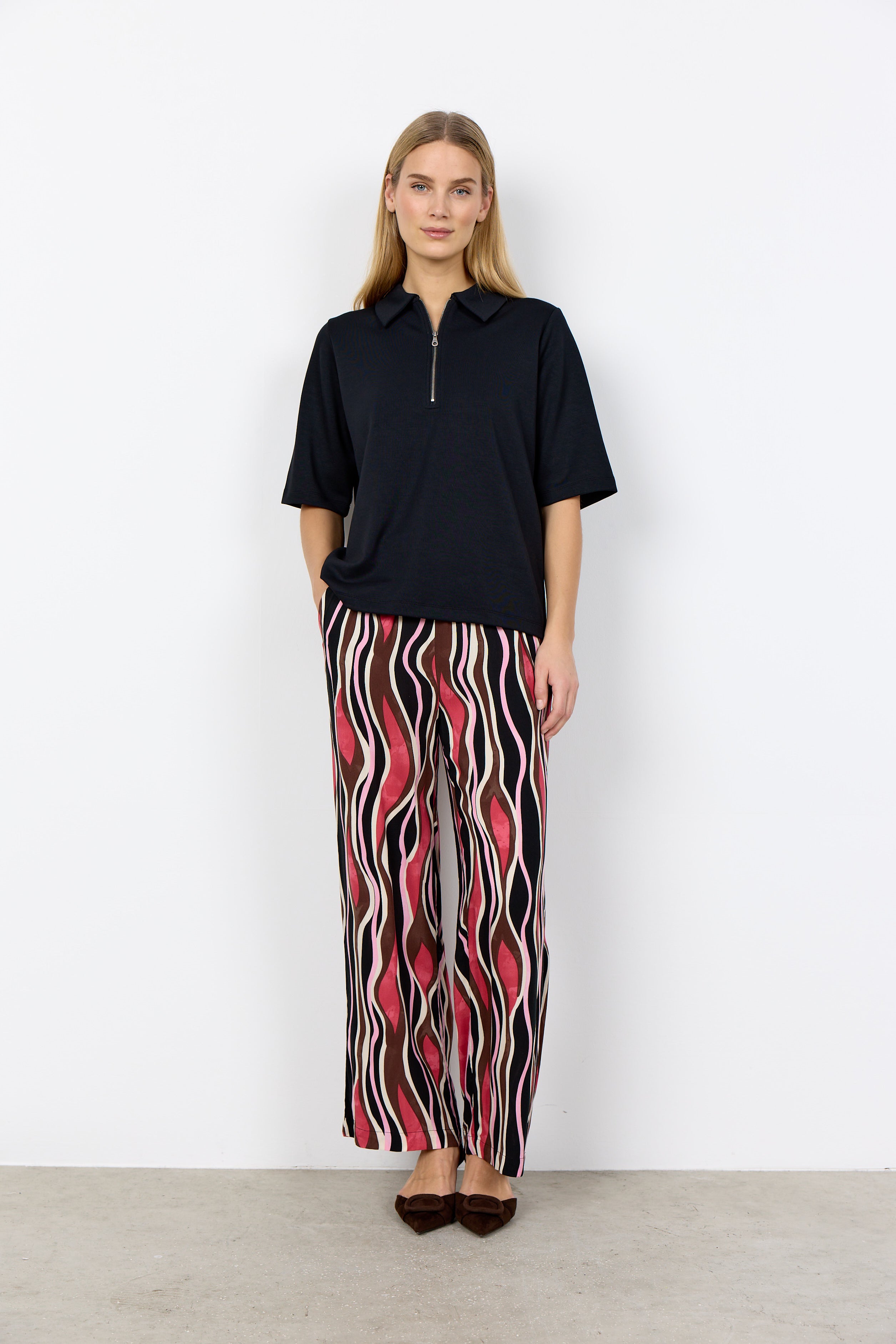 Woman wearing a black polo shirt and patterned pants against a white background