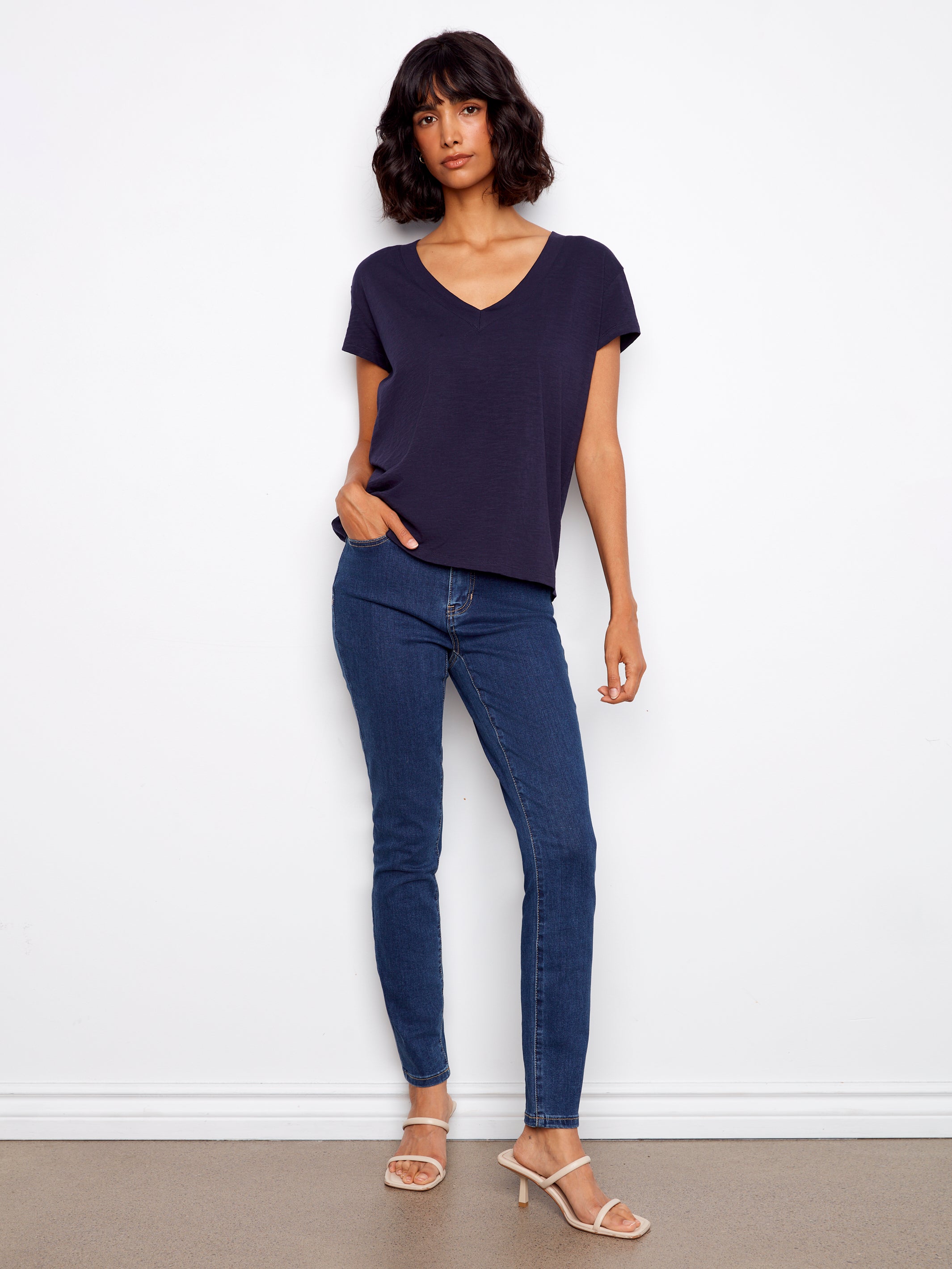 Woman wearing a navy blue t-shirt and jeans against a white wall