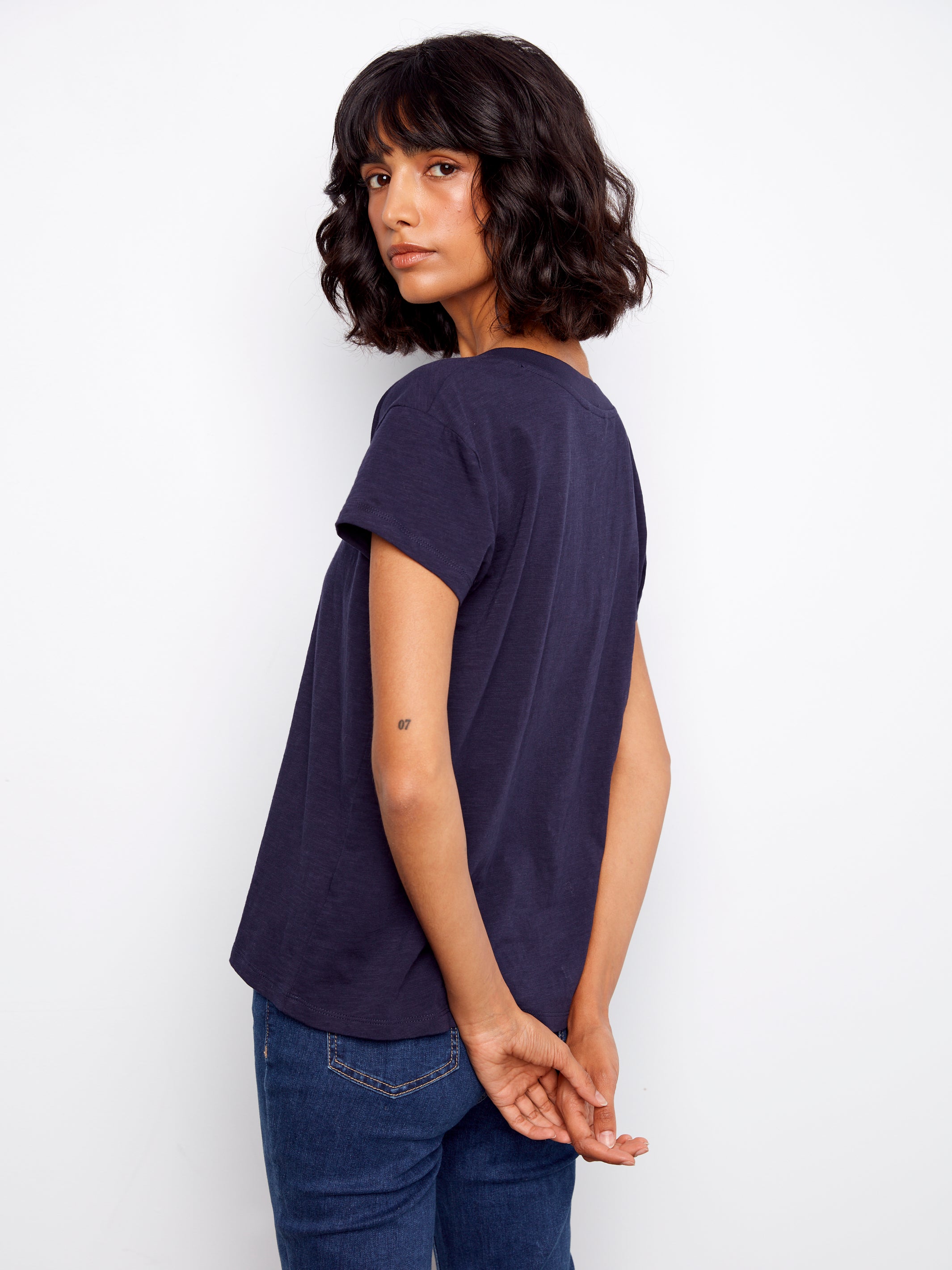 Woman wearing a navy blue t-shirt and jeans against a white background