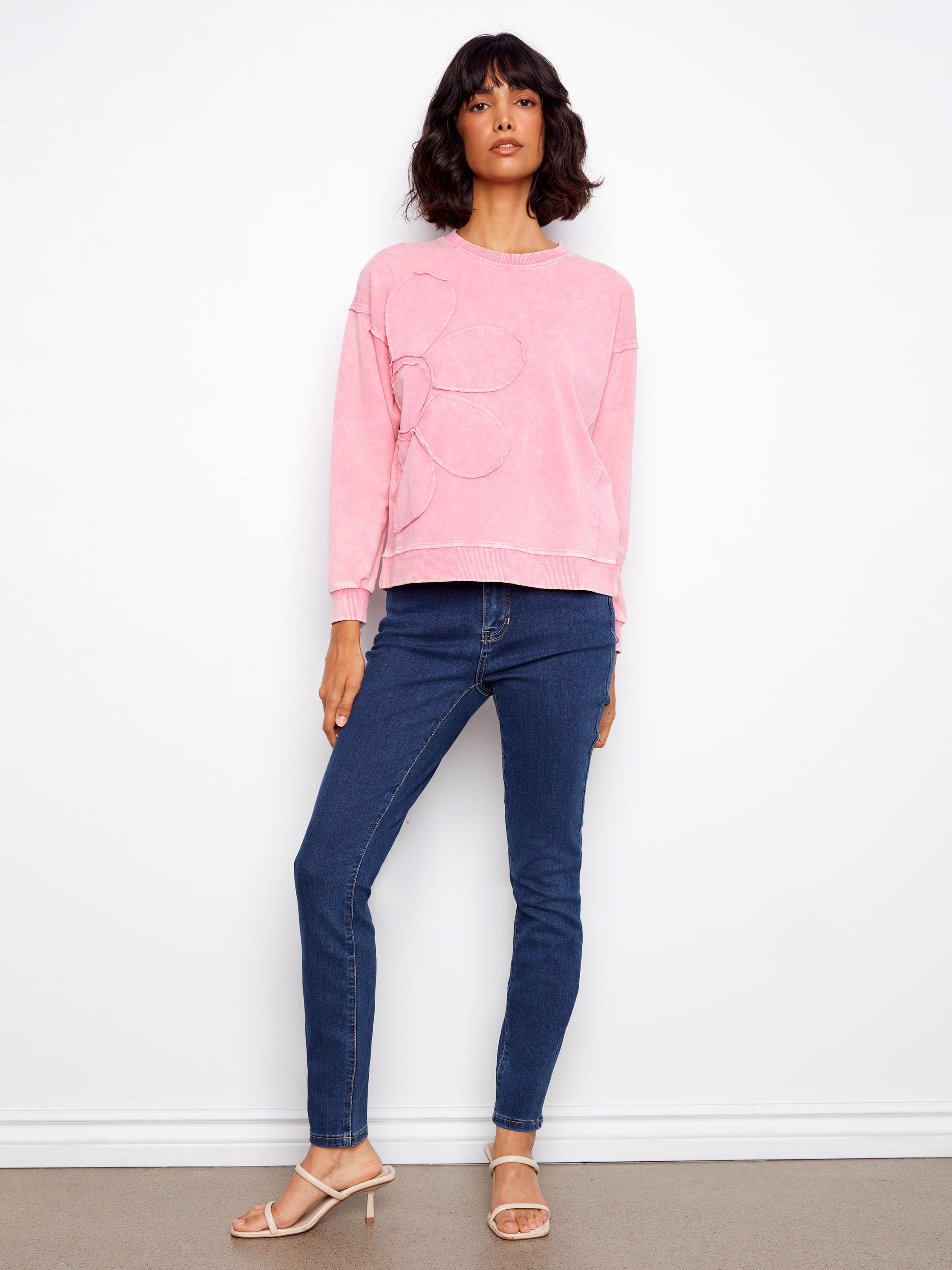 Woman wearing a pink sweatshirt and blue jeans against a white background