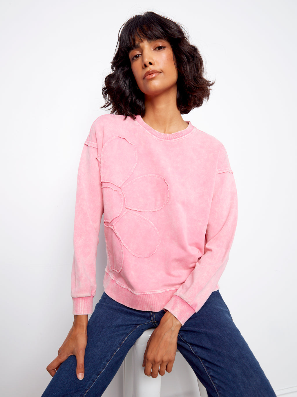 Woman wearing a pink sweatshirt and blue jeans against a white background