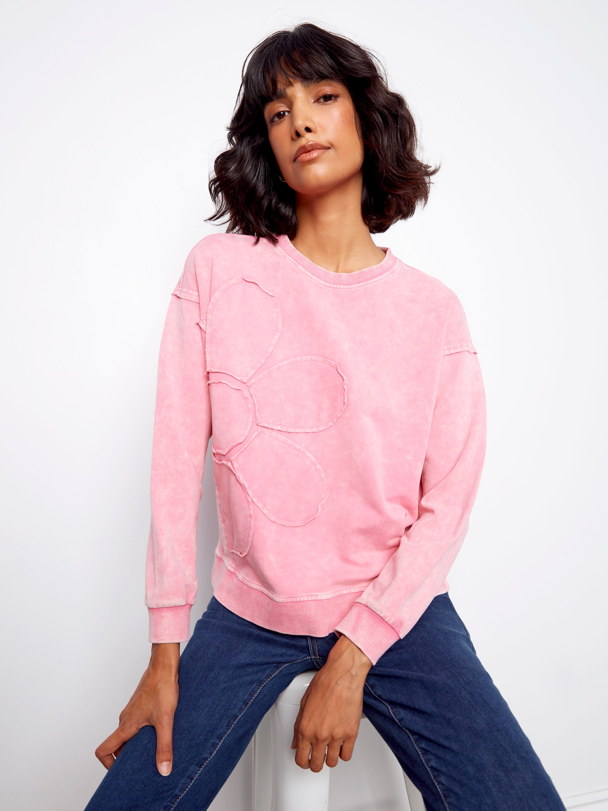 Woman wearing a pink sweatshirt and blue jeans against a white background