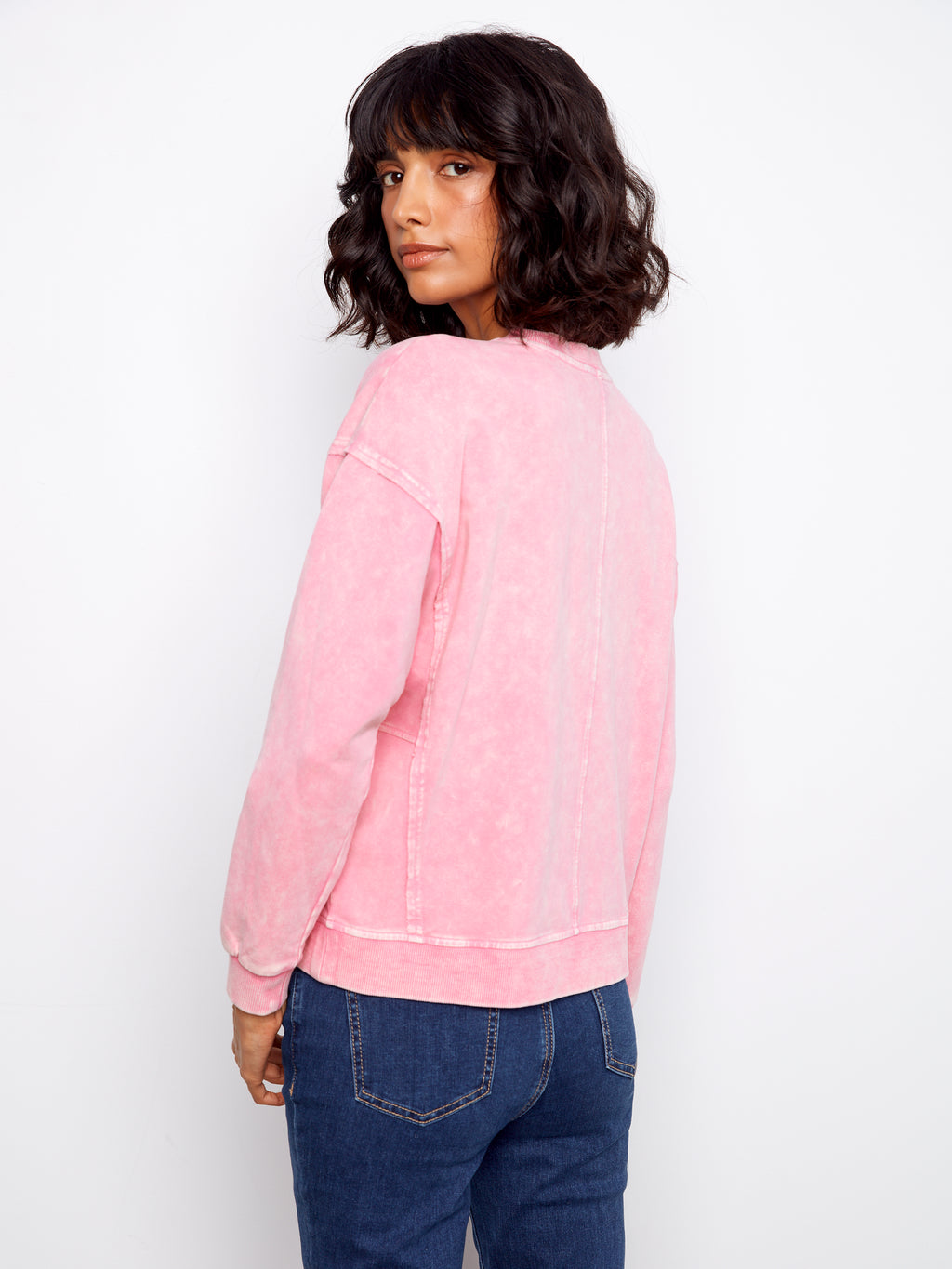 Person wearing a pink sweatshirt and blue jeans against a white background