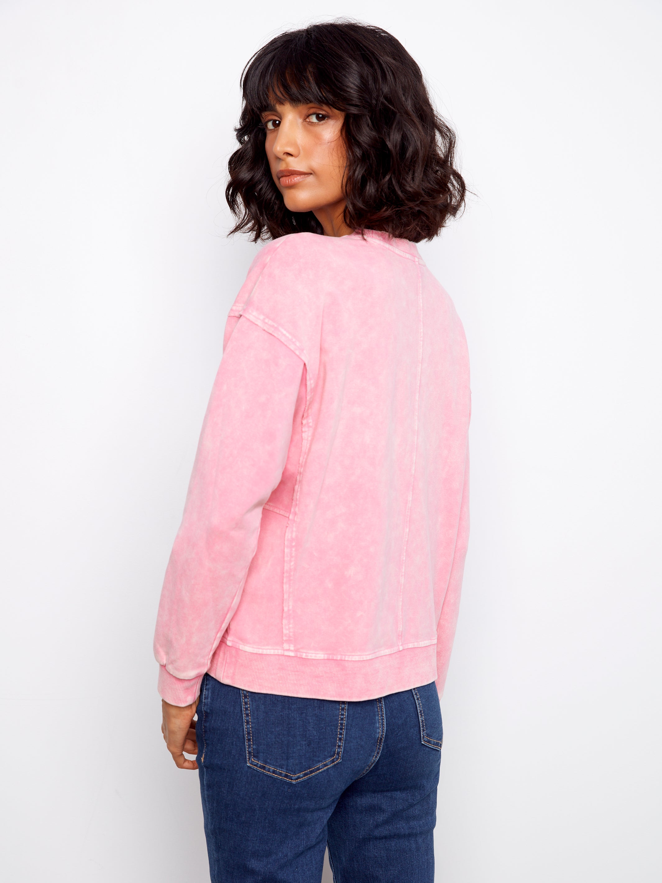 Person wearing a pink sweatshirt and blue jeans against a white background