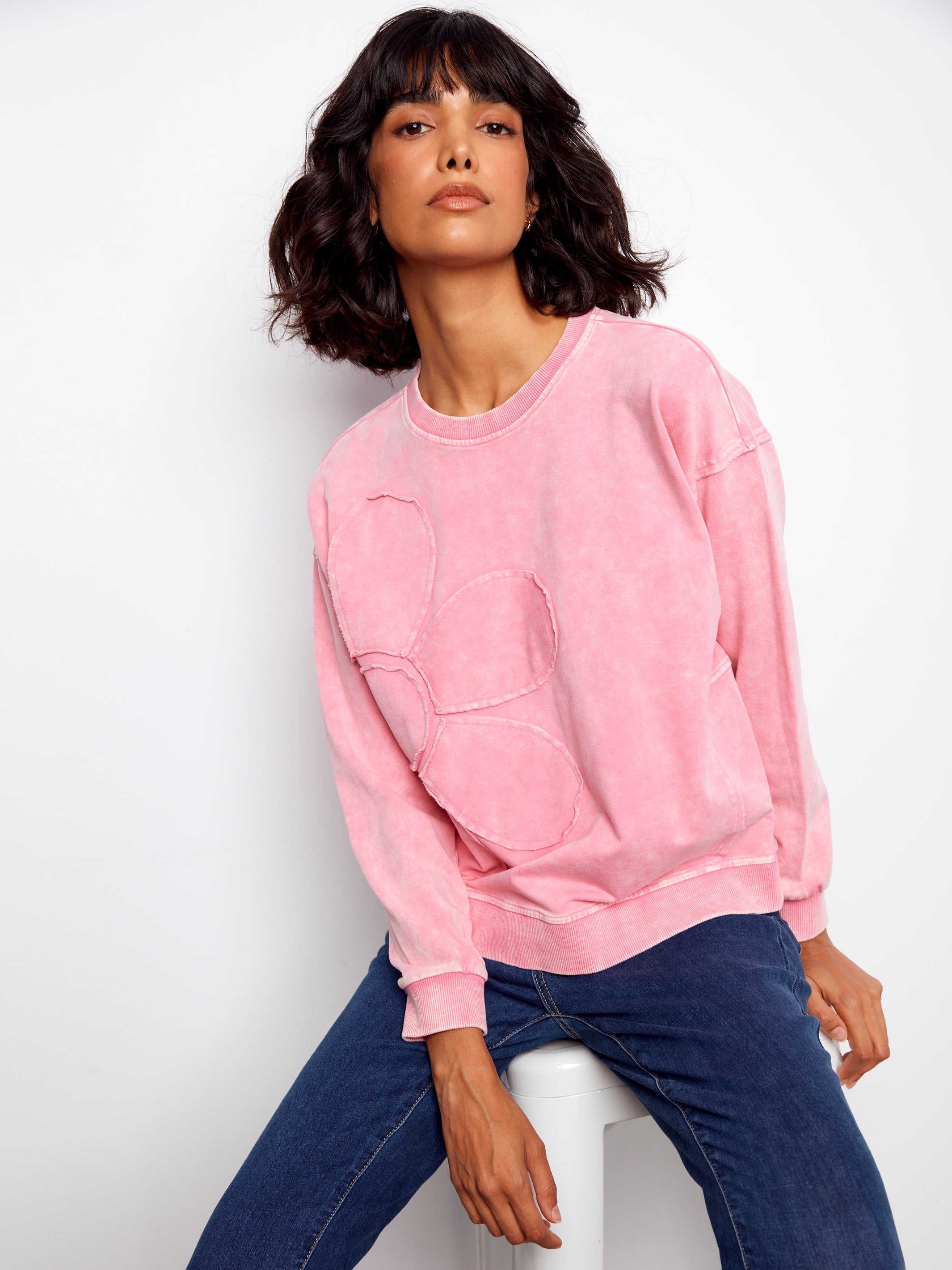 Woman wearing a pink sweatshirt and blue jeans against a white background