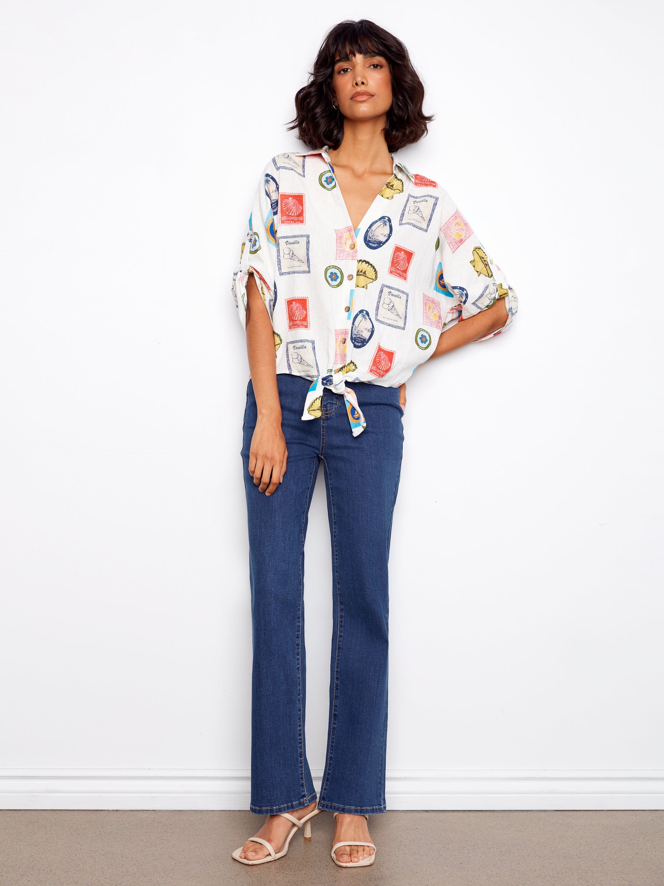 Woman wearing a patterned blouse and blue jeans against a white background