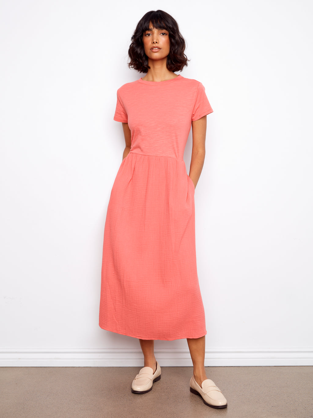 Woman wearing a coral dress standing against a white wall.
