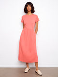 Woman wearing a coral dress standing against a white wall.