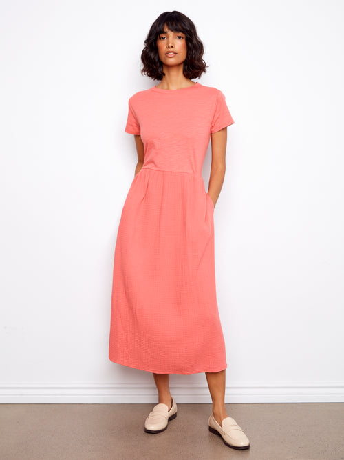Woman wearing a coral dress standing against a white wall.