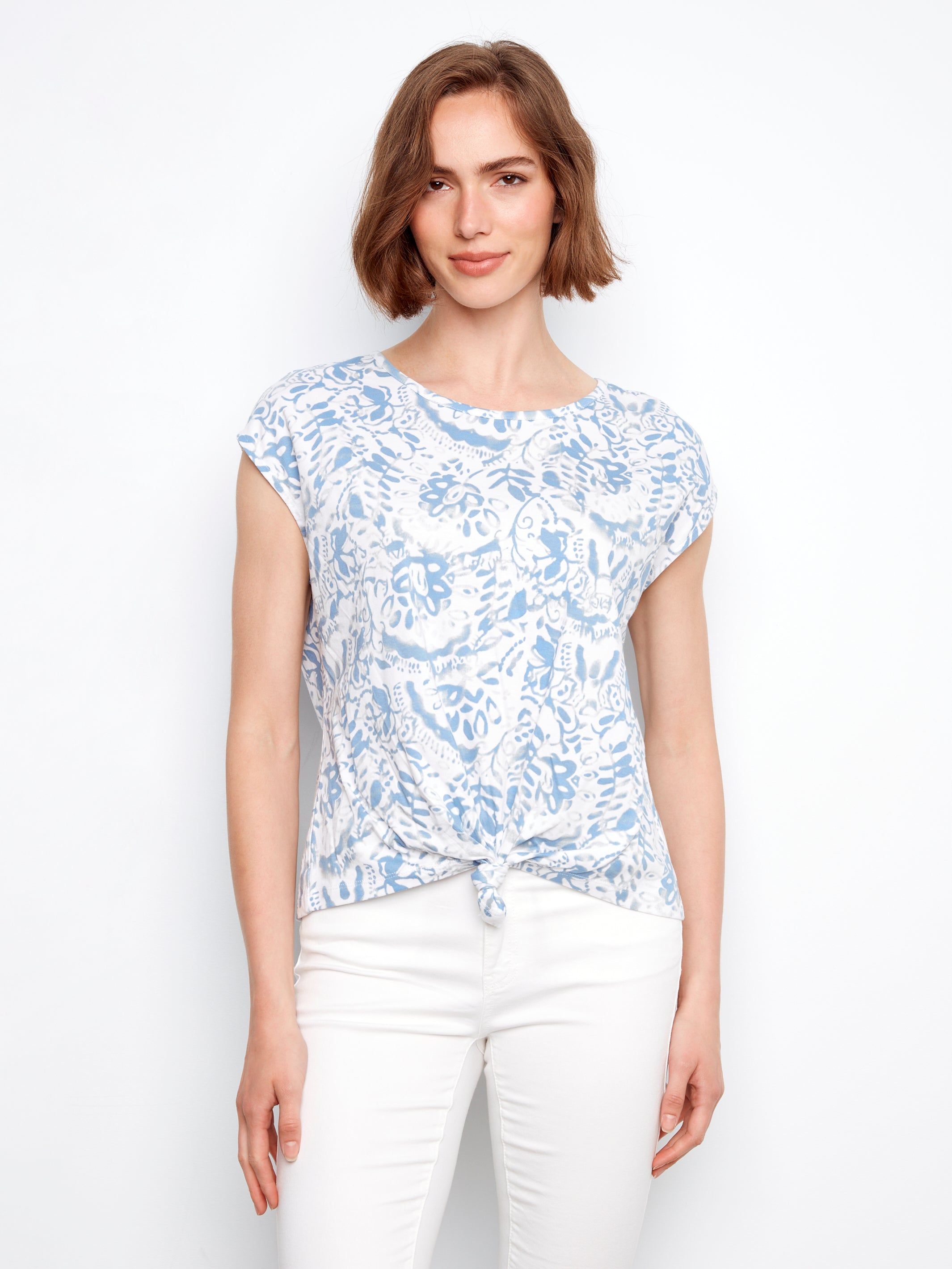 Woman wearing a blue floral top and white pants on a white background