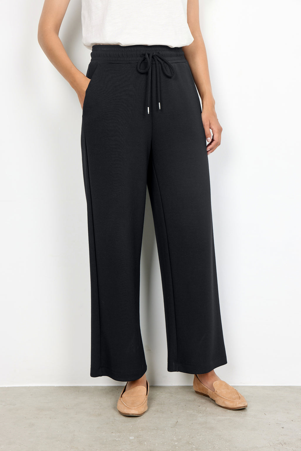 Person wearing black wide-leg pants with a white top against a plain background