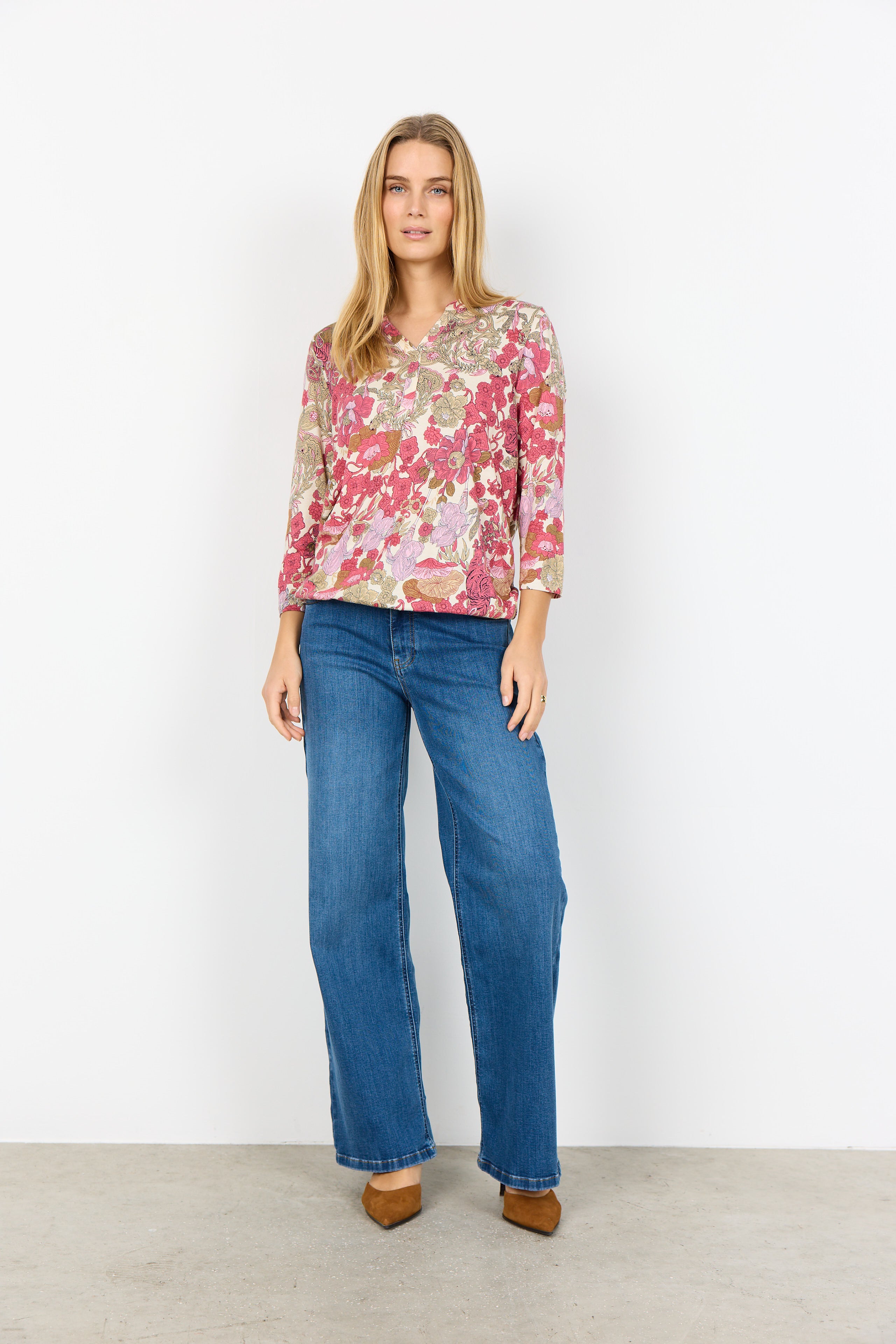 Woman wearing a floral blouse and blue jeans against a white background