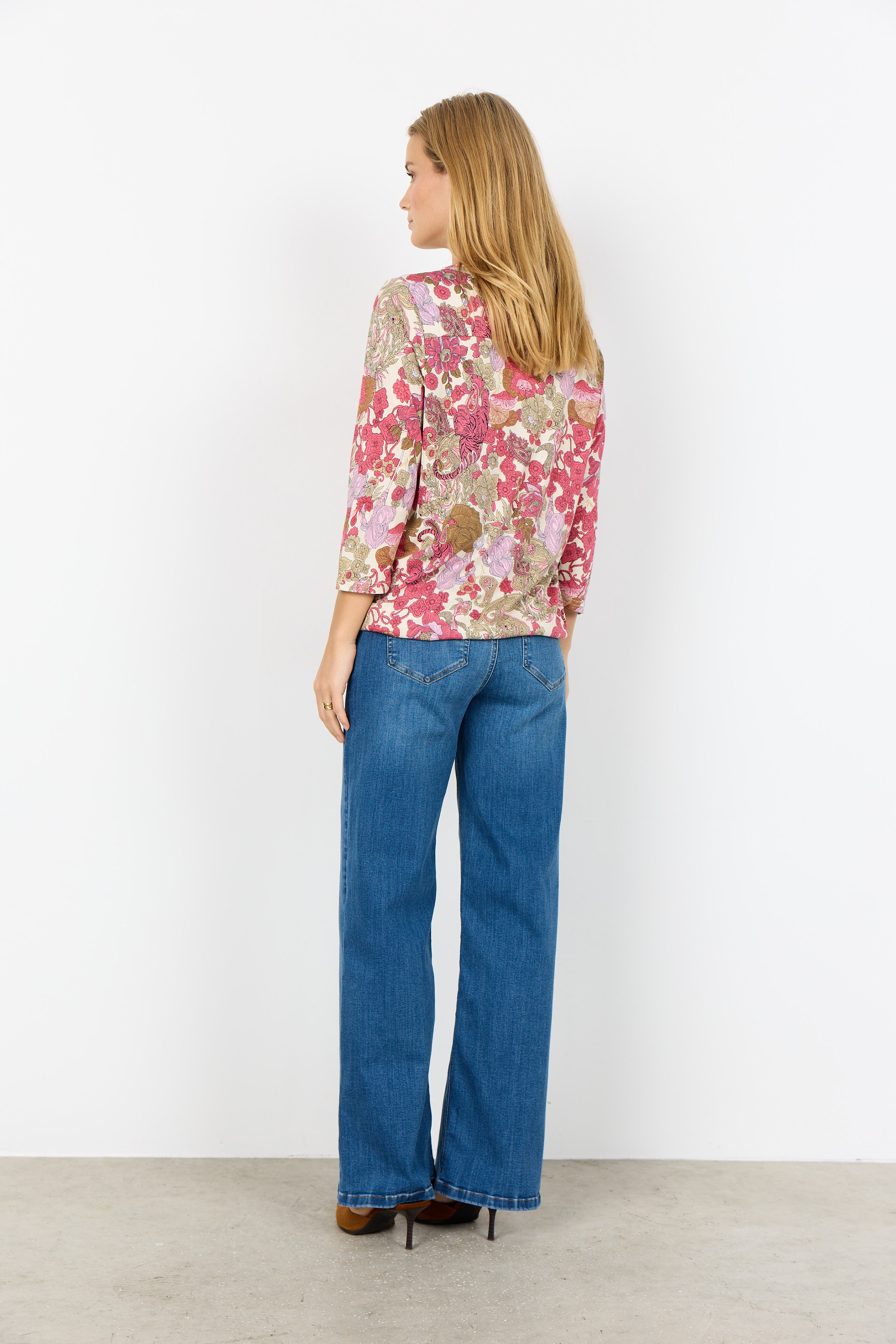 Woman wearing a floral blouse and blue jeans against a white background