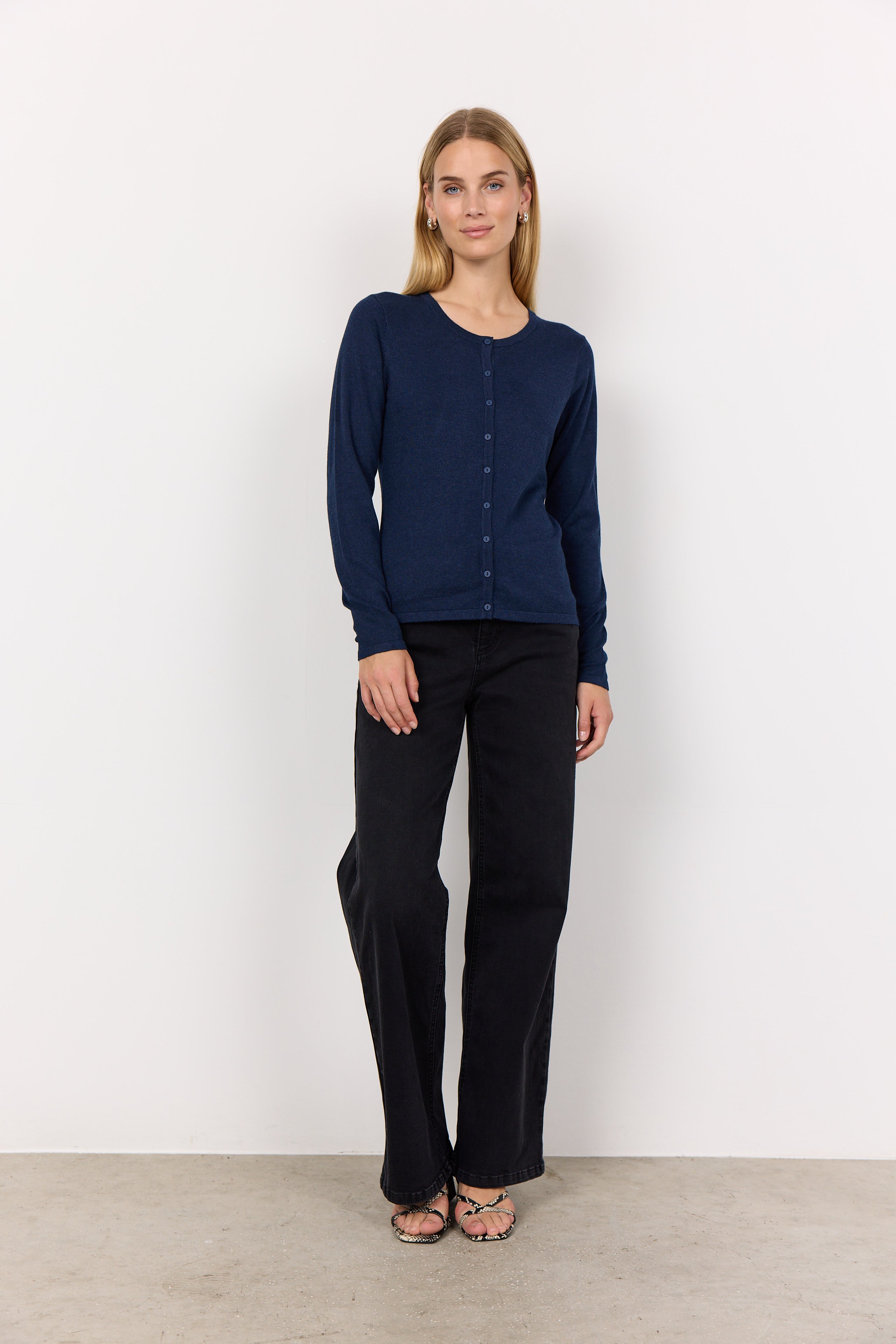 Woman wearing a navy blue cardigan and black pants against a white background