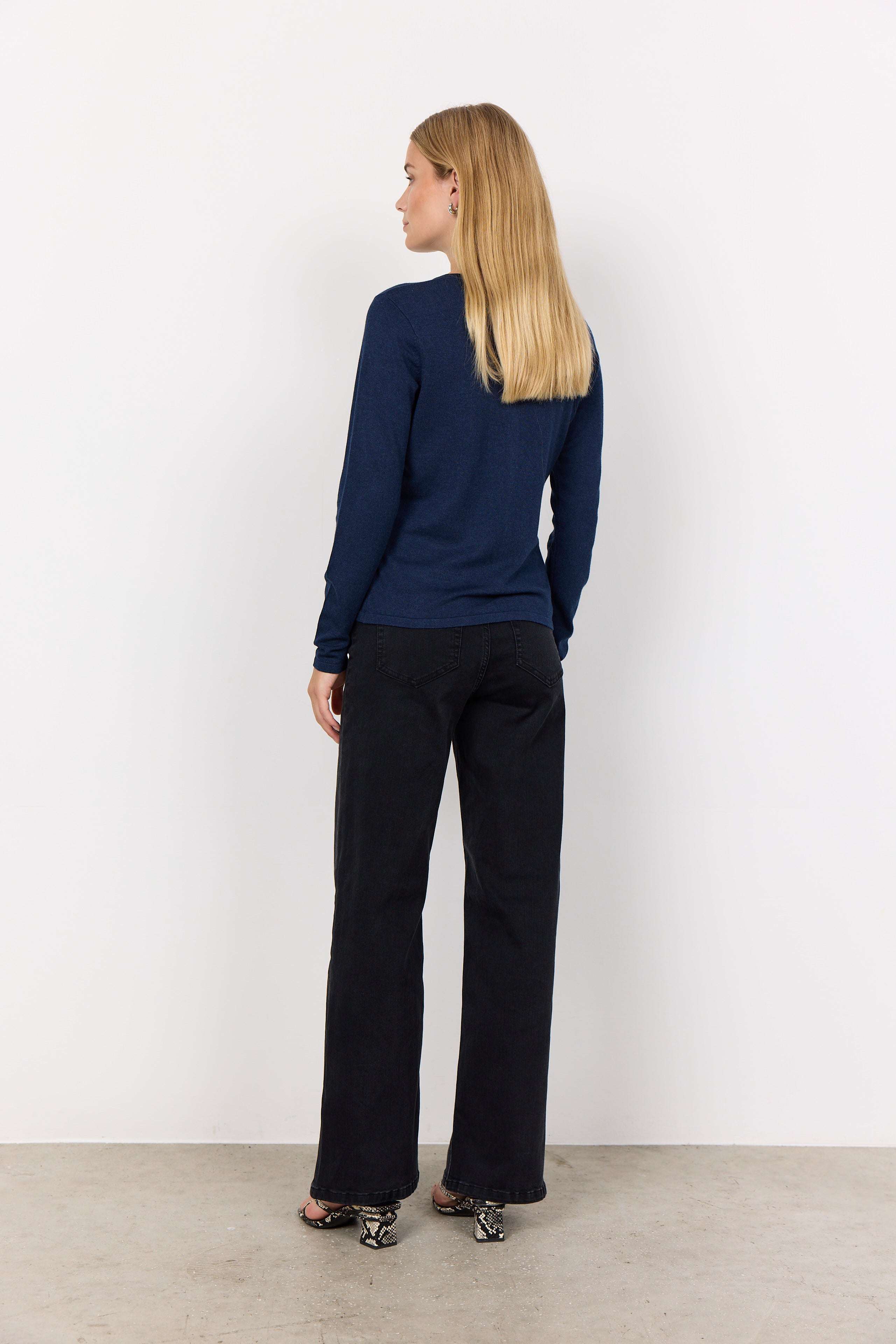Person wearing a navy sweater and black pants against a white background