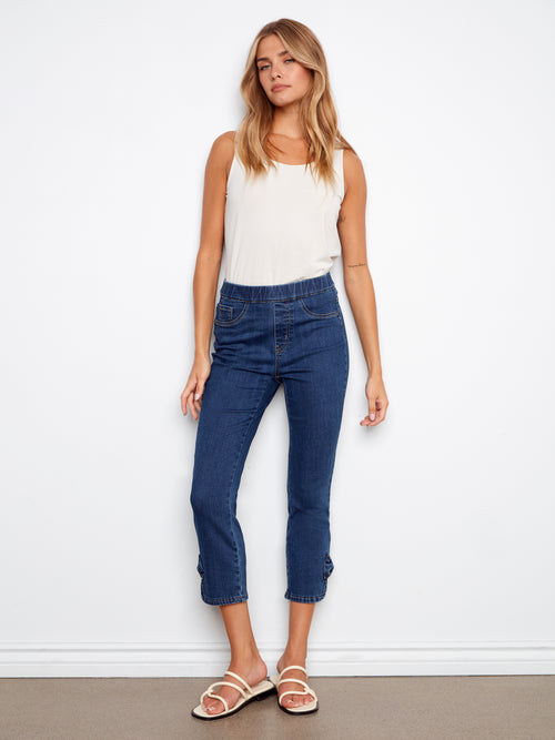 Woman wearing a white tank top and blue jeans against a white background