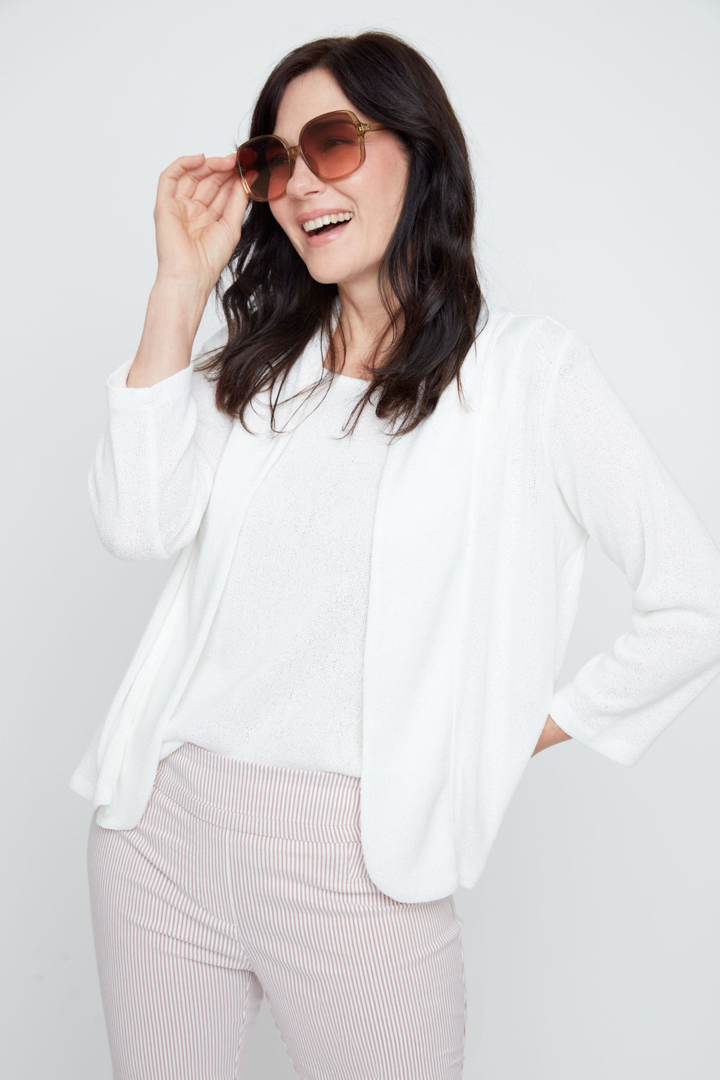 Woman wearing a white blazer and sunglasses on a plain background