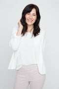 Woman wearing a white blouse and light pink pants against a plain background