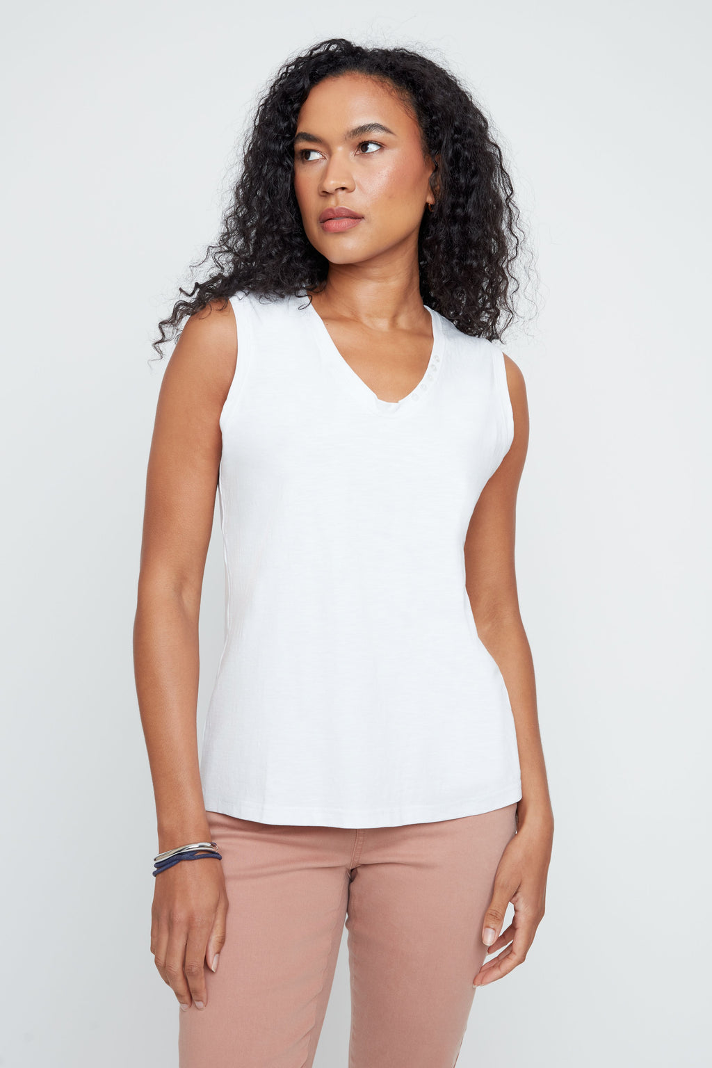 Woman wearing a white sleeveless top and pink pants against a plain background