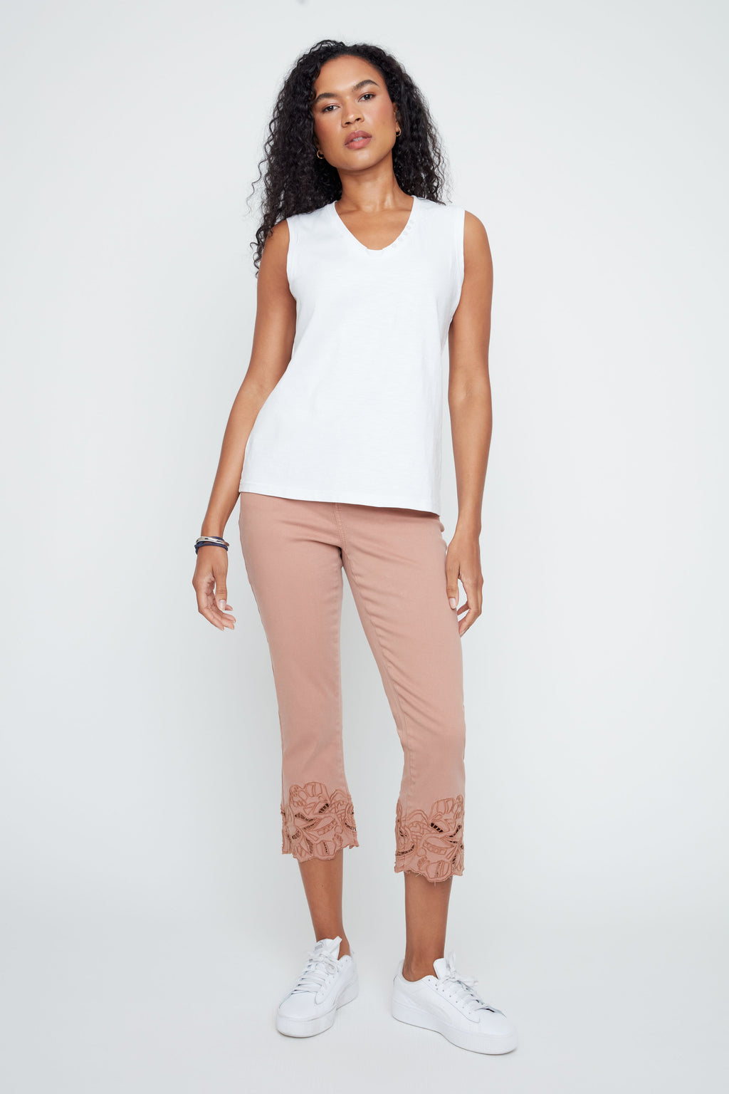 Woman wearing a white sleeveless top and pink pants with lace details on a white background