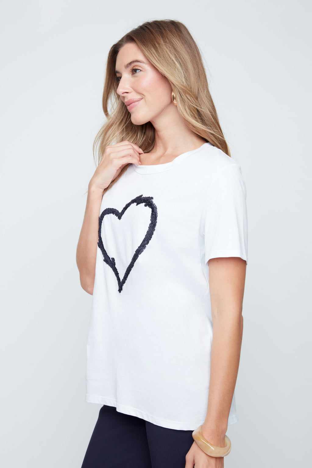 Woman wearing a white t-shirt with a black heart design on a plain background